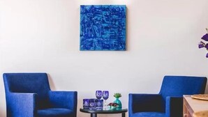 Ein Zimmer mit zwei blauen Stühlen, einem kleinen runden Tisch mit Dekoration und einem blauen abstrakten Gemälde an der Wand.