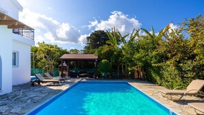 Ein Swimmingpool mit Liegestühlen, einer Grillmöglichkeit und üppiger Bepflanzung.