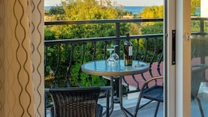 Ein Balkon mit Glastisch, zwei Korbstühlen, einer Flasche und einem Weinglas.