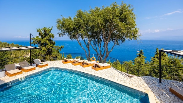 A pool with lounge chairs and a view of the sea.