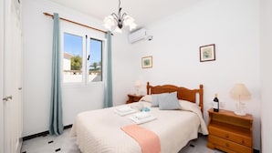A bedroom with a bed, bedside tables, a window with curtains, a ceiling light, and wall-mounted air conditioning.
