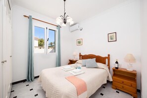 Une chambre à coucher comprenant un lit, des tables de chevet, une fenêtre avec des rideaux, un luminaire au plafond et un climatiseur fixé au mur.