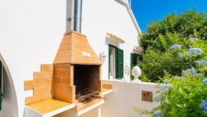 A white building with a brick-built outdoor oven, green shutters, and a clear blue sky.