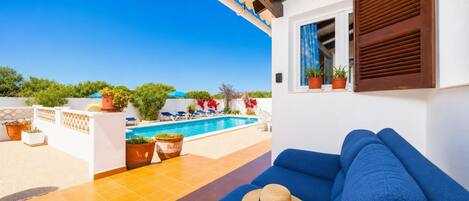 Un sofá azul con un sombrero de paja, una piscina y macetas con plantas en una terraza.