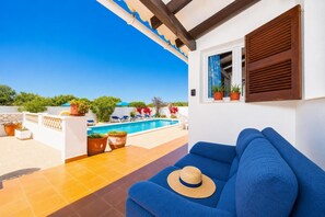Ein blaues Sofa, ein Strohhut, ein Pool und Kübelpflanzen auf einer Terrasse.