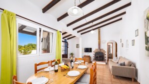 A dining area with a wooden table set for four, a sofa, a TV, and a fireplace. - Villa Ca Nostra - Three Bedroom Villa, Sleeps 6 (Cala en Porter)