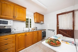 Une cuisine avec des meubles de rangement en bois, un four à micro-ondes, un évier, un lave-vaisselle et un panier de fruits posé sur le comptoir.