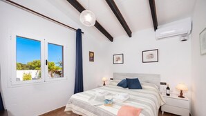 A bedroom with a bed, two bedside tables, a window, and an air conditioning unit. - Villa Ca Nostra - Three Bedroom Villa, Sleeps 6 (Cala en Porter)