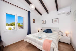 Une chambre à coucher comprenant un lit, deux tables de chevet, une fenêtre et un appareil de climatisation.