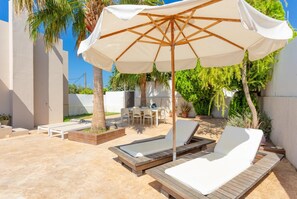 A sunlit outdoor area with lounge chairs, a table, and an umbrella.
