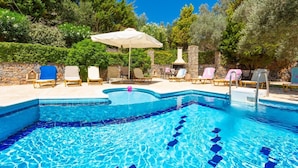 Une piscine dont les bords sont recouverts de carreaux, entourée de chaises longues et d’un mur en pierre.
