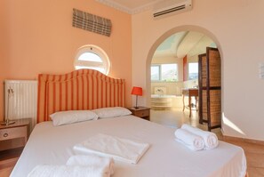 A hotel room with a large bed, a nightstand, a lamp, a radiator, and an arched doorway leading to a bathroom. - Villa Pelagos - Five Bedroom Villa, Sleeps 10 (Agia Triada)