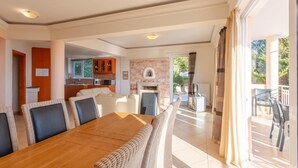 Un vaste espace de vie comprenant une table à manger en bois, des sièges confortables, une cuisine à l’arrière-plan et un balcon aménagé avec du mobilier d’extérieur.
