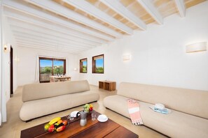 En rummelig opholdsstue med to sofaer, et sofabord med frugt og et spiseområde med et bord og stole.
