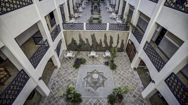 A courtyard with a central decorative tile pattern, surrounded by white tables and chairs, and potted plants. - Batha (Fes)