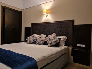 A hotel room with a large bed, dark headboard, patterned pillows, a bedside lamp, and a nightstand. - Batha (Fes)