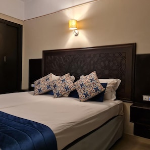 A hotel room with a large bed, a headboard with intricate patterns, and a wall-mounted light fixture. - Batha (Fes)