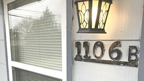 Le numéro de maison, 1106B, est peint en blanc sur le mur extérieur, à côté d’une fenêtre et d’une lanterne fixée au mur.