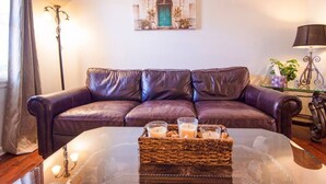 Un salon avec un canapé en cuir, une table basse en verre ornée de bougies et un tableau encadré accroché au mur.