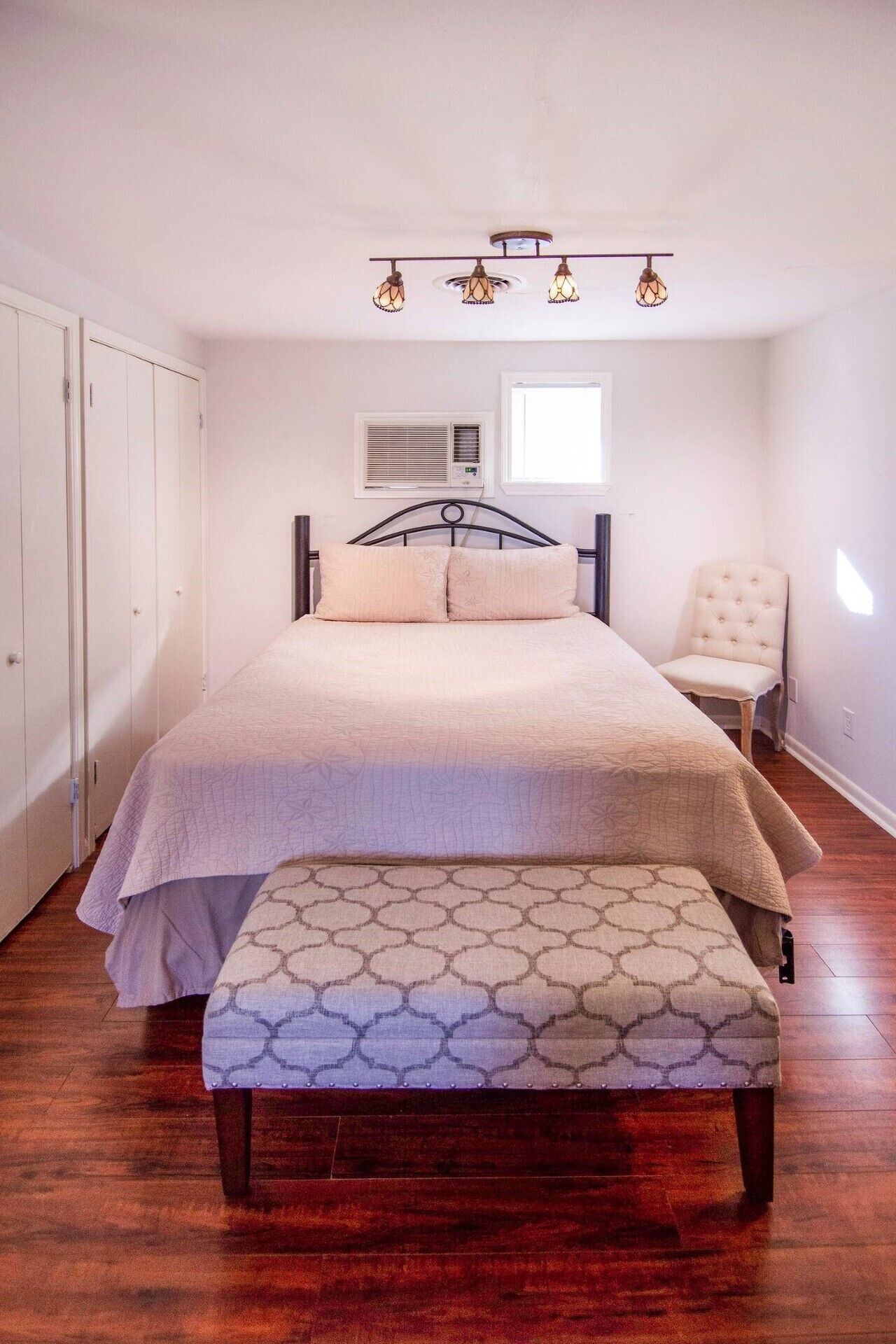 A bedroom with a bed, a bench, a chair, and a ceiling light fixture.