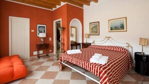 Ein Hotelzimmer mit Schachbrettfußboden, einem Bett mit gestreifter Bettdecke, einer Holzzieldecke und einer Tür.