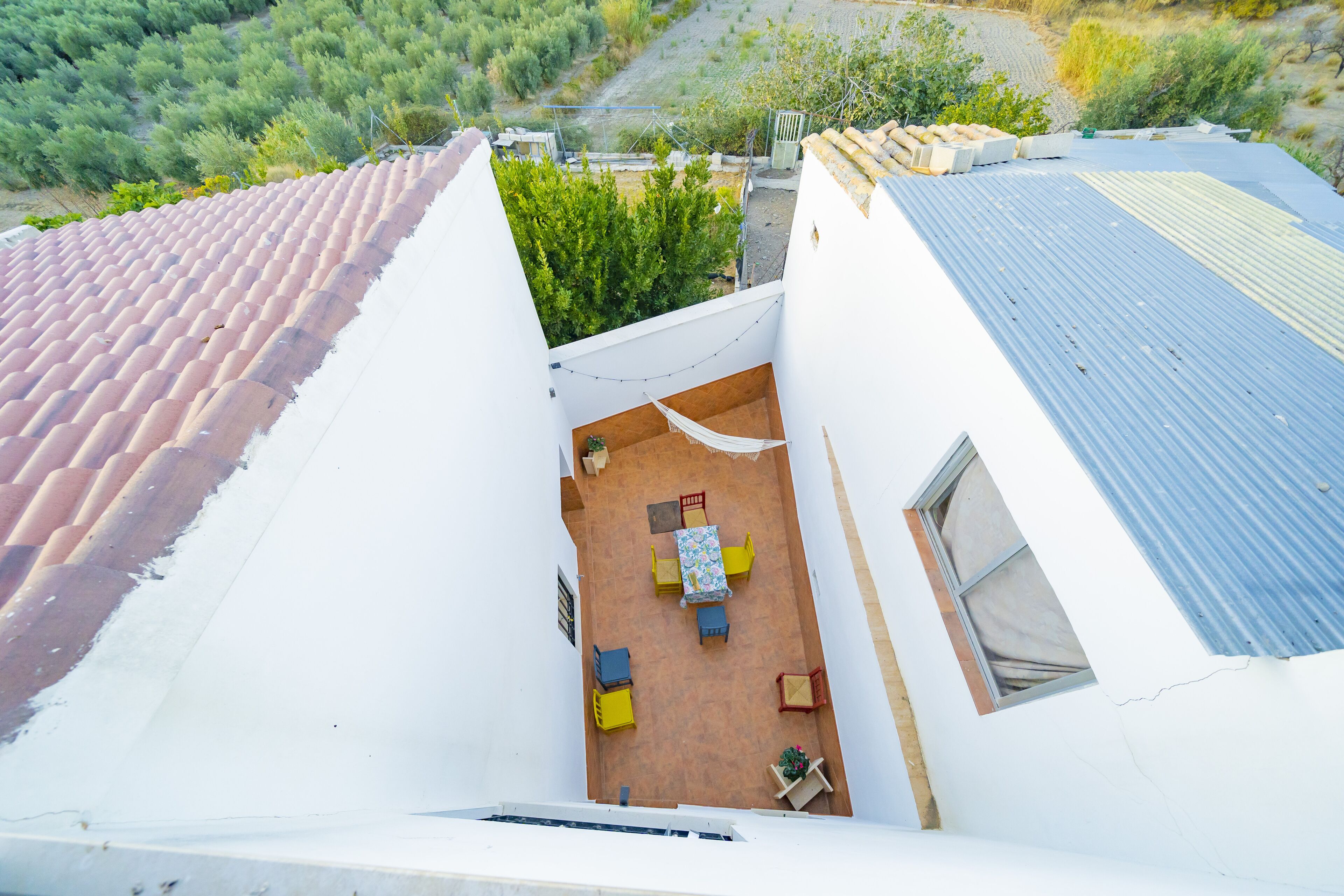 Une terrasse sur le toit, avec une table et des chaises, entourée de murs blancs et surmontée d’un toit recouvert de tuiles rouges.