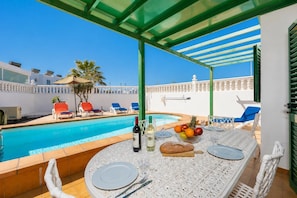 Zona de comedor junto a la piscina con una mesa para dos, una botella de vino y un bol de fruta.
