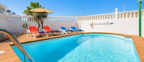 A swimming pool with lounge chairs and a sun umbrella.