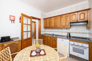 A compact kitchen with wooden cabinets, a granite countertop, and a dining area with a patterned tablecloth.