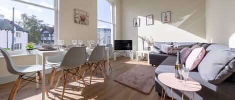 Una sala moderna con comedor, un sofá gris y una televisión.