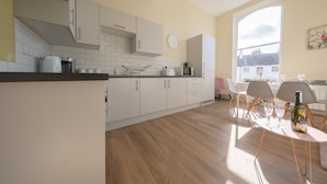 Eine moderne Küche mit weißen Schränken, einer Holz Arbeitsplatte und einem Essbereich mit Tisch für zwei Personen.