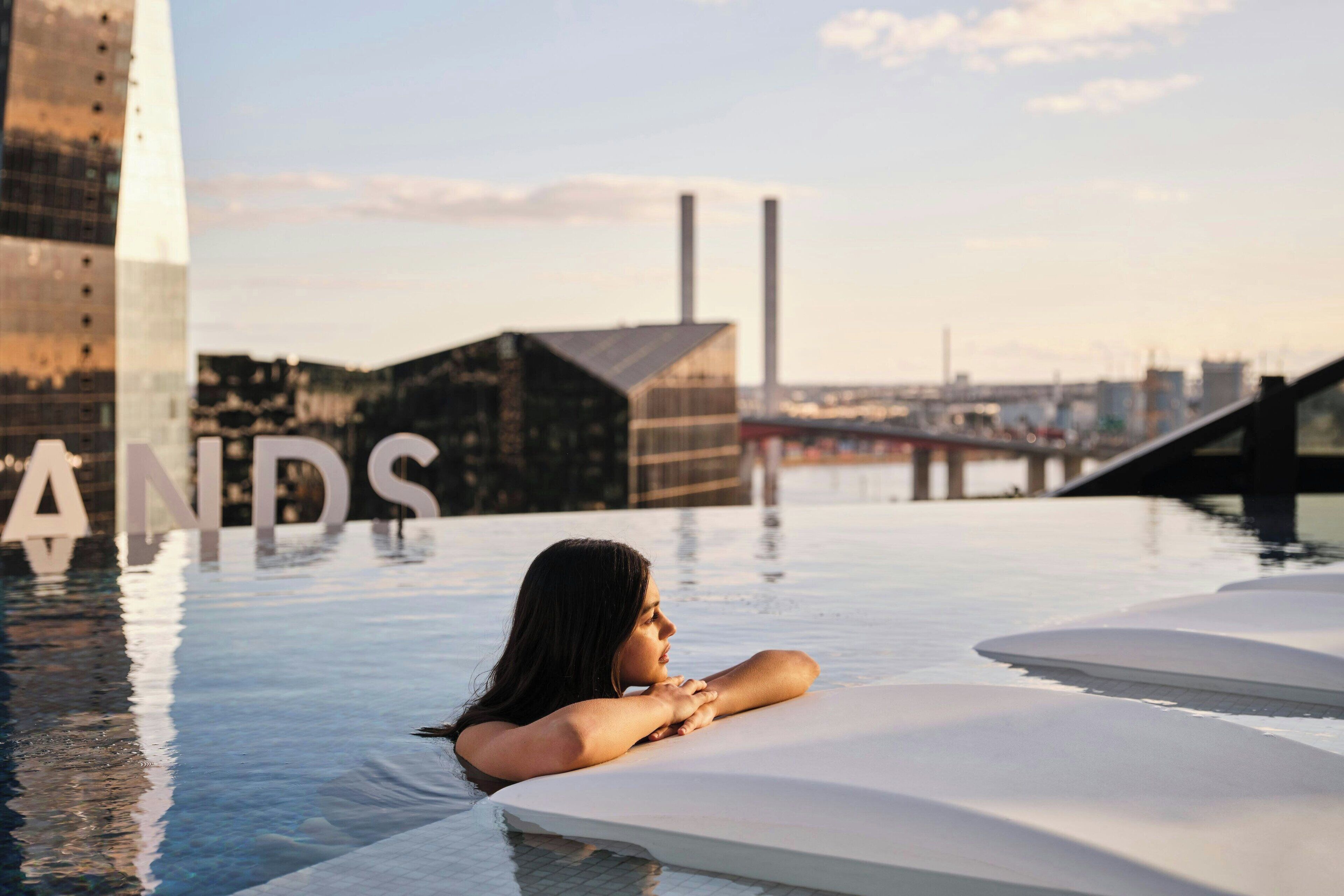 A person relaxing in a modern infinity pool with a cityscape in the background.