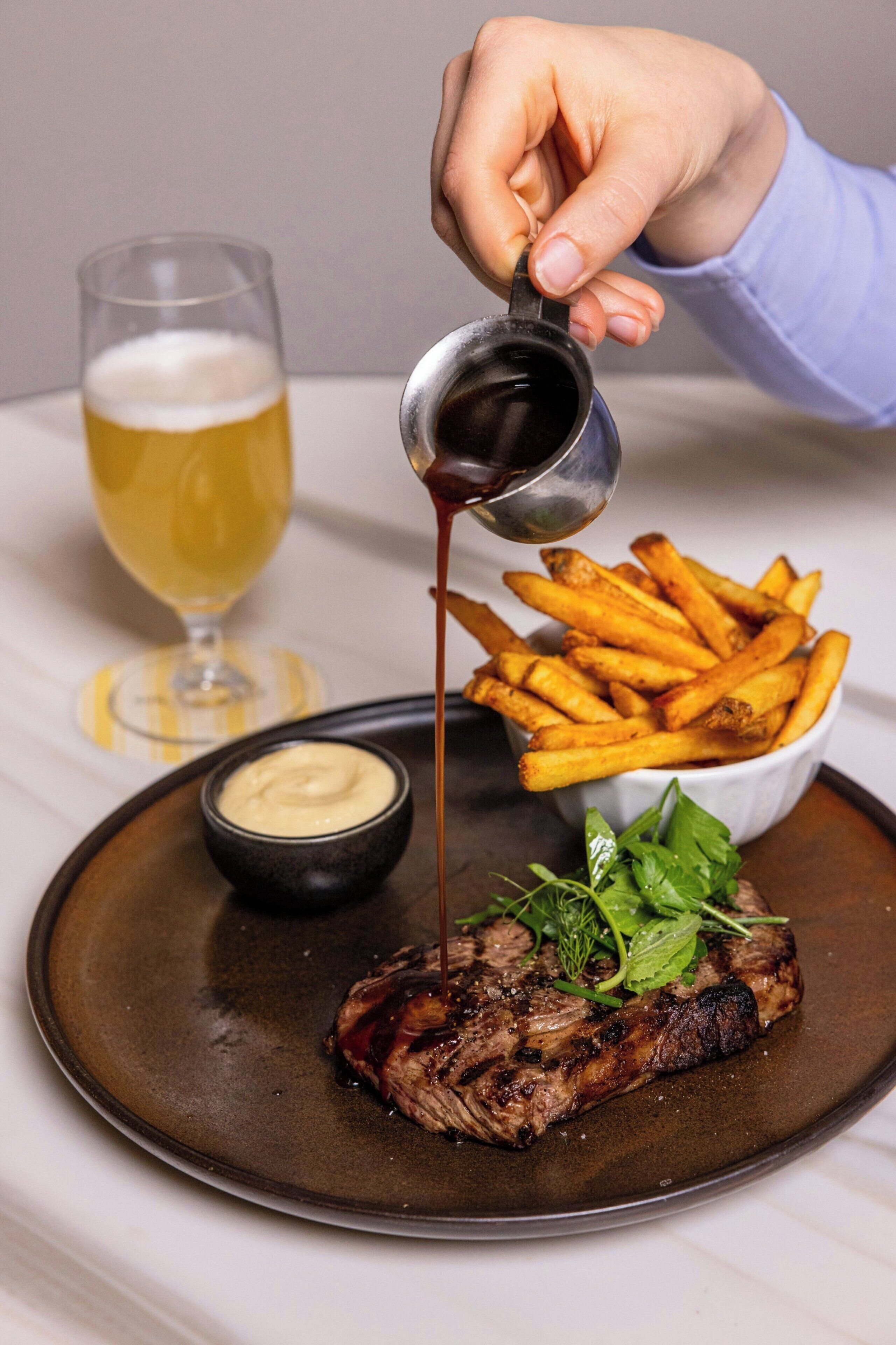 A steak with fries and a glass of beer on a plate.
