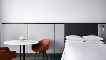 A modern hotel room with a bed, a round table with two chairs, and a small vase with flowers.