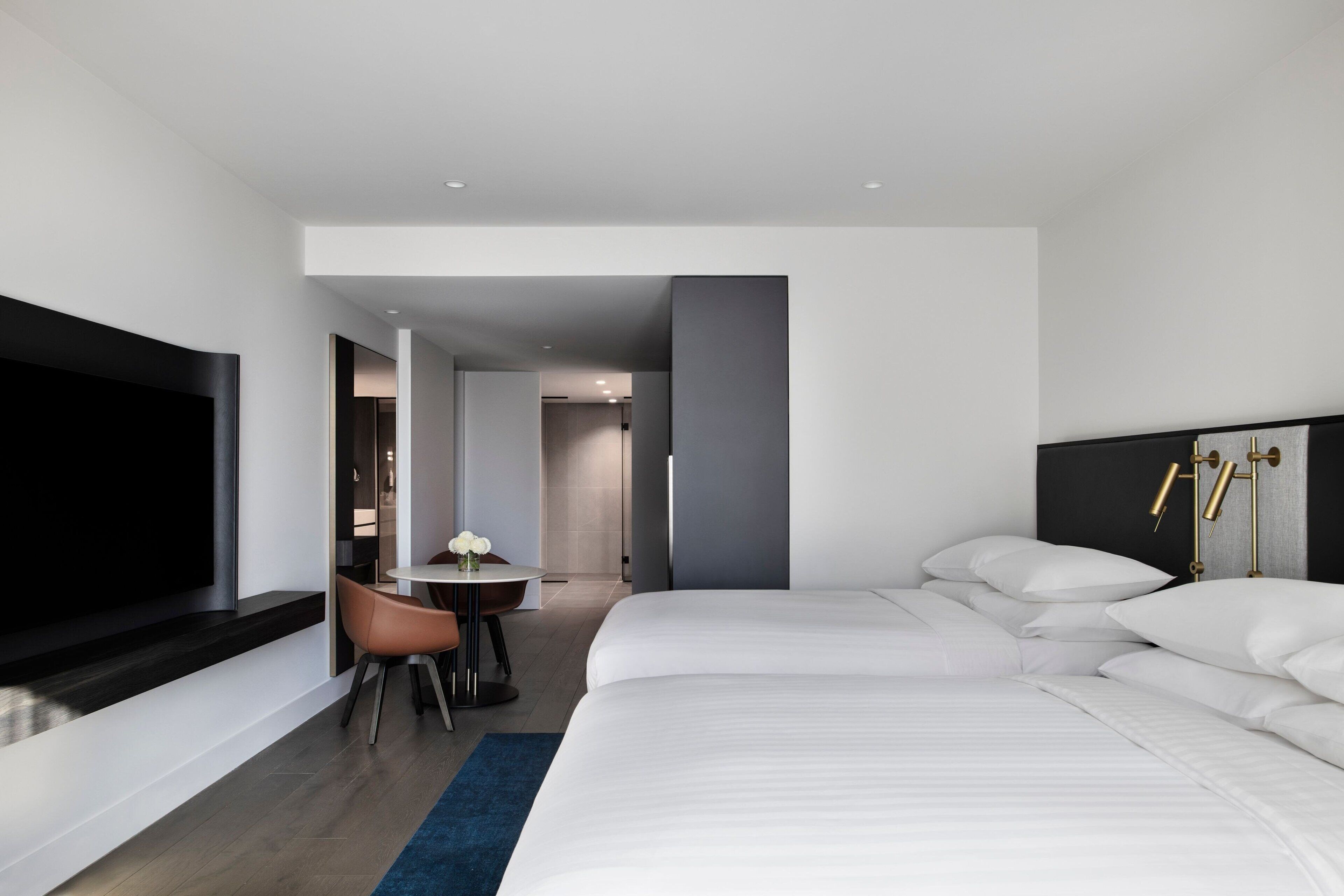 A modern hotel room with a large bed, a flat-screen TV, a small dining table, and a chair.