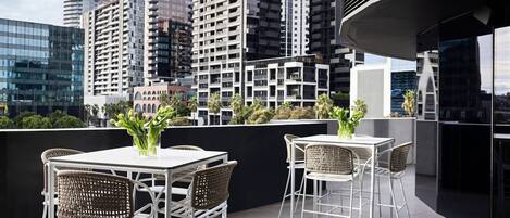 A rooftop terrace with white metal furniture and a view of surrounding high-rise buildings.