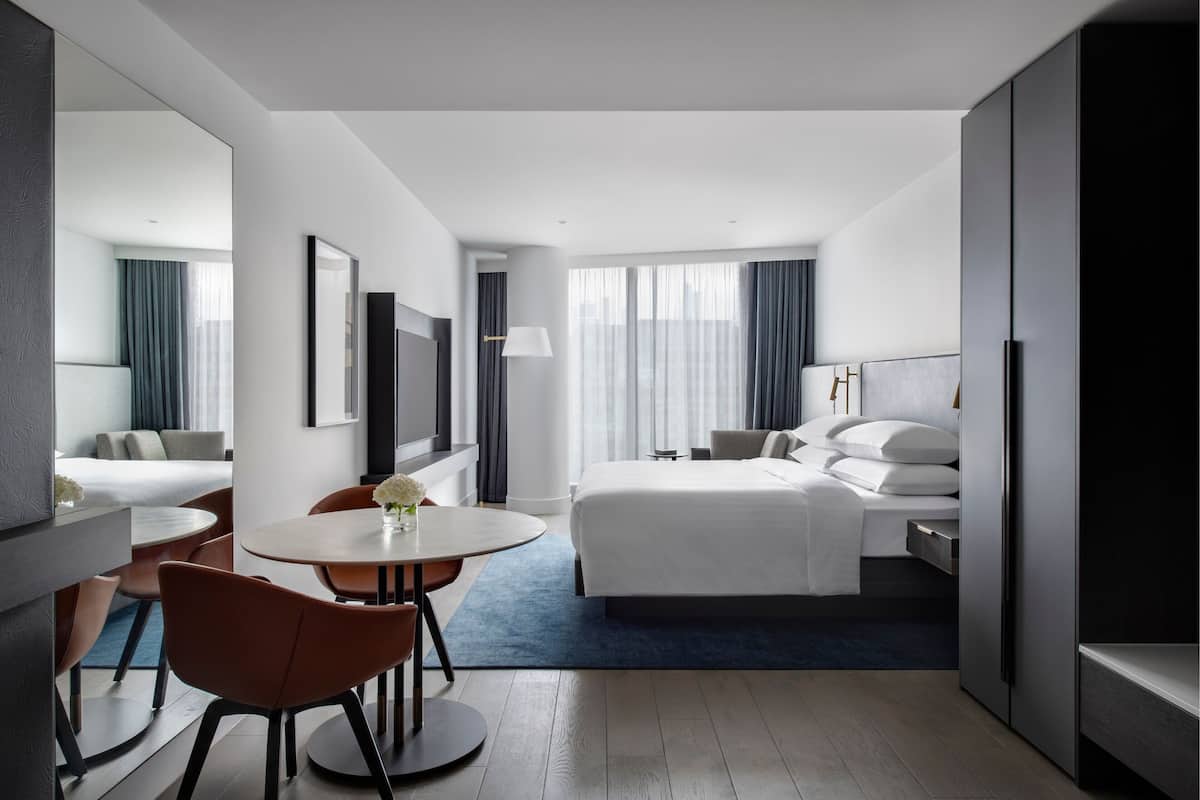 A modern hotel room with a bed, a desk, a chair, and a dining table.