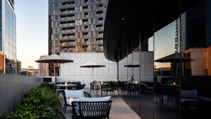 An outdoor dining area with tables and chairs, surrounded by greenery and modern buildings in the background. - Melbourne Marriott Hotel Docklands (Docklands)