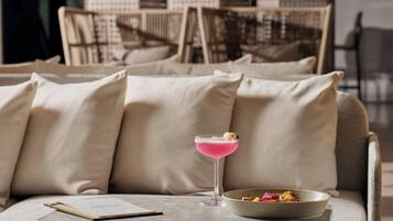 A seating area with a table, a cocktail glass, a bowl of food, and a menu on a clipboard.