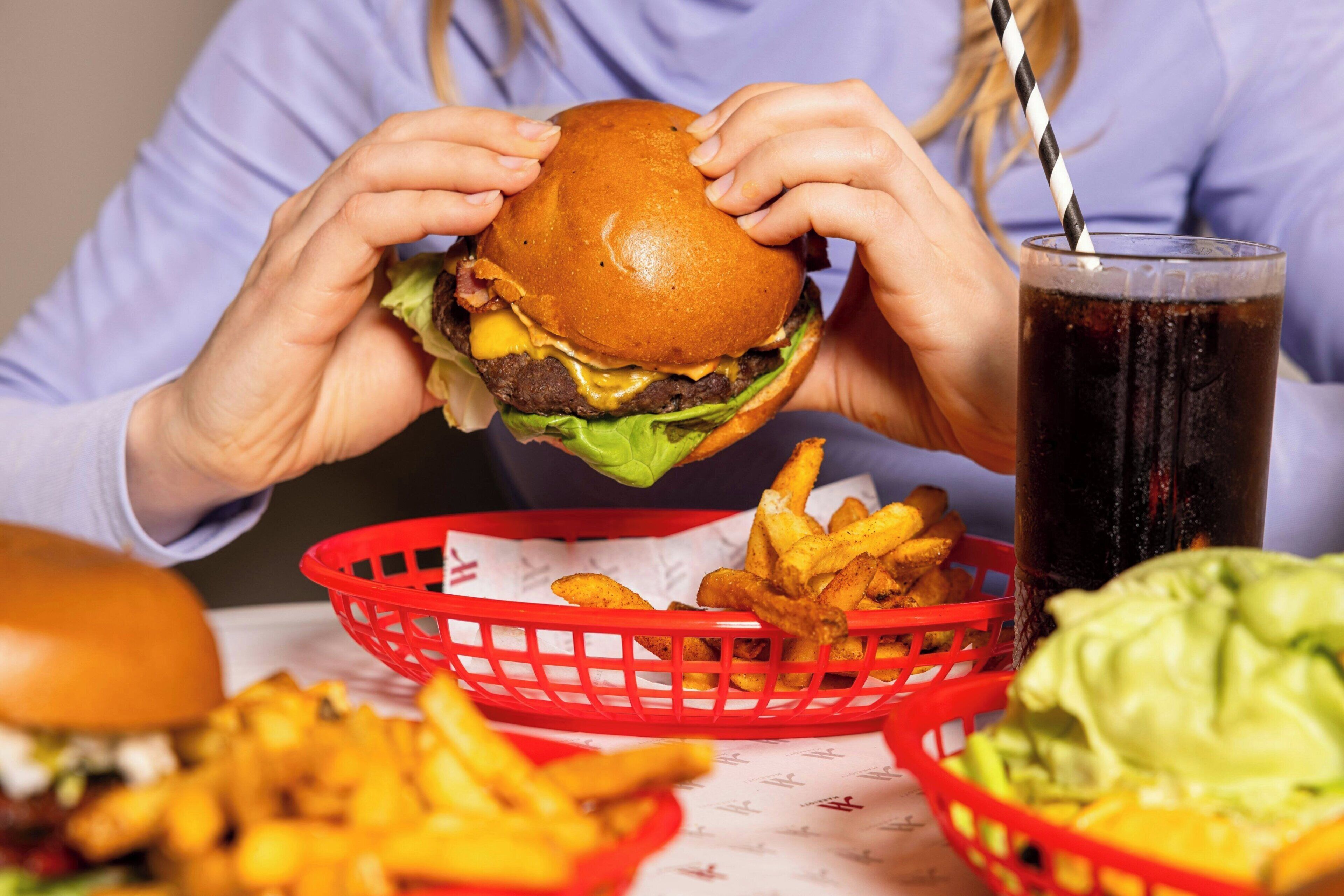 Una persona sosteniendo una hamburguesa, una cesta de papas fritas y una bebida.
