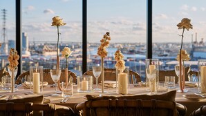 A dining table set with candles, glassware, and a view of a cityscape through large windows.