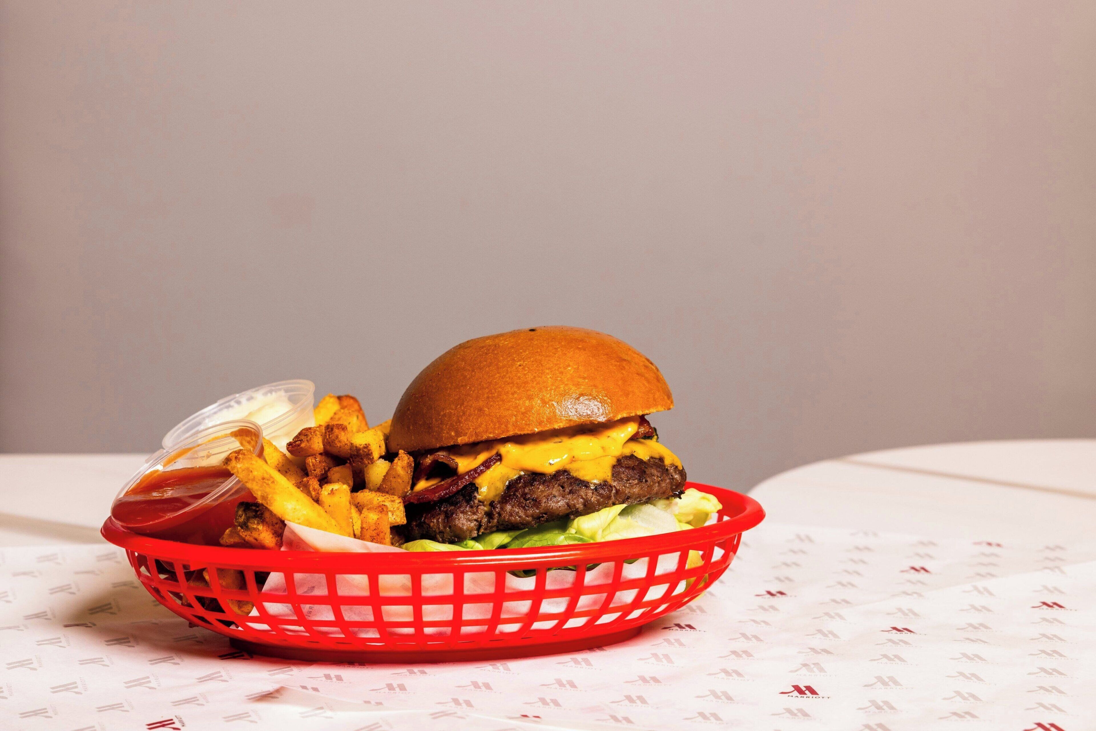 Un panier contenant un hamburger, des frites et une boisson, posé sur une table.