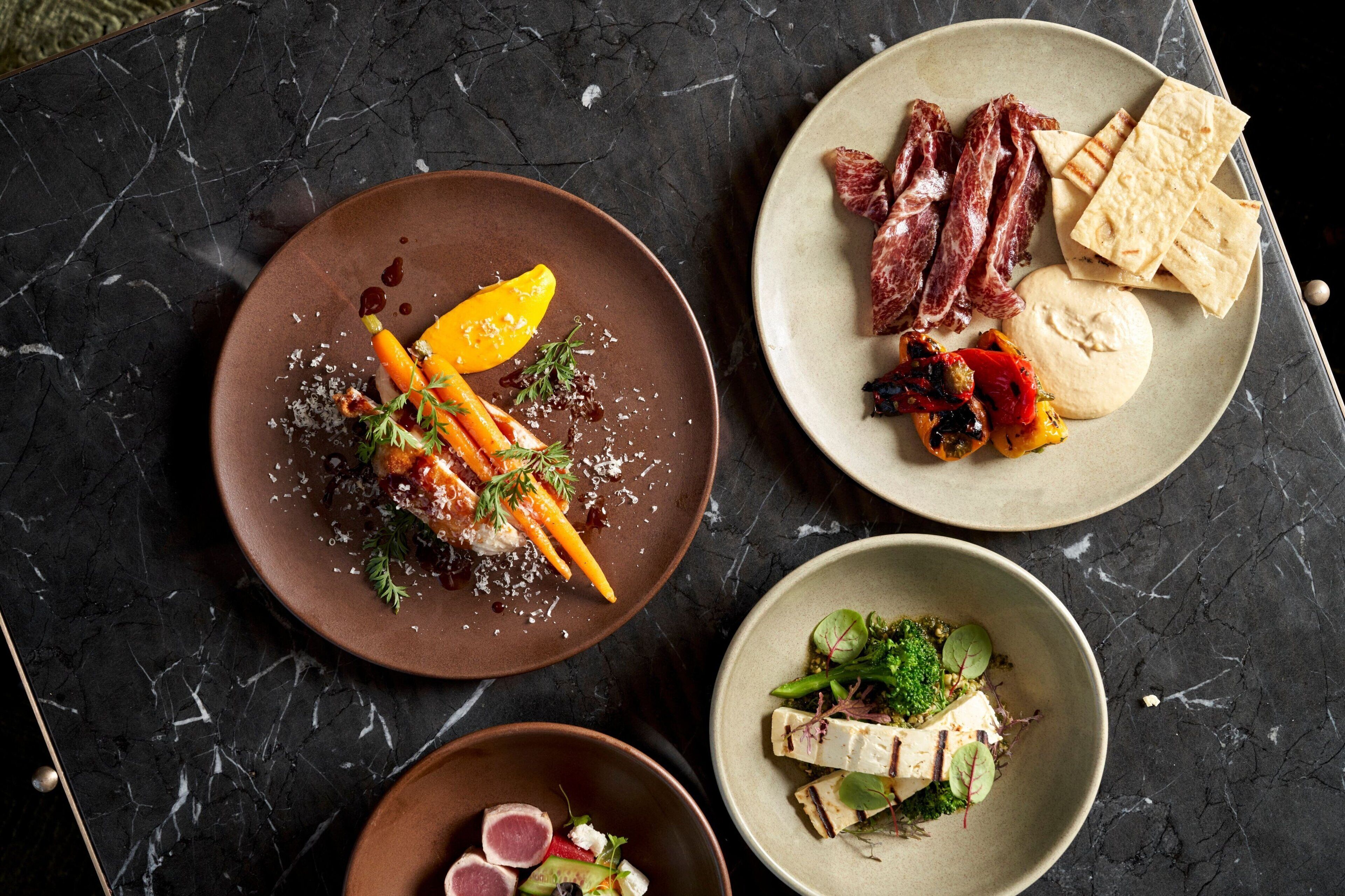 Three plates of food on a dark marble table.