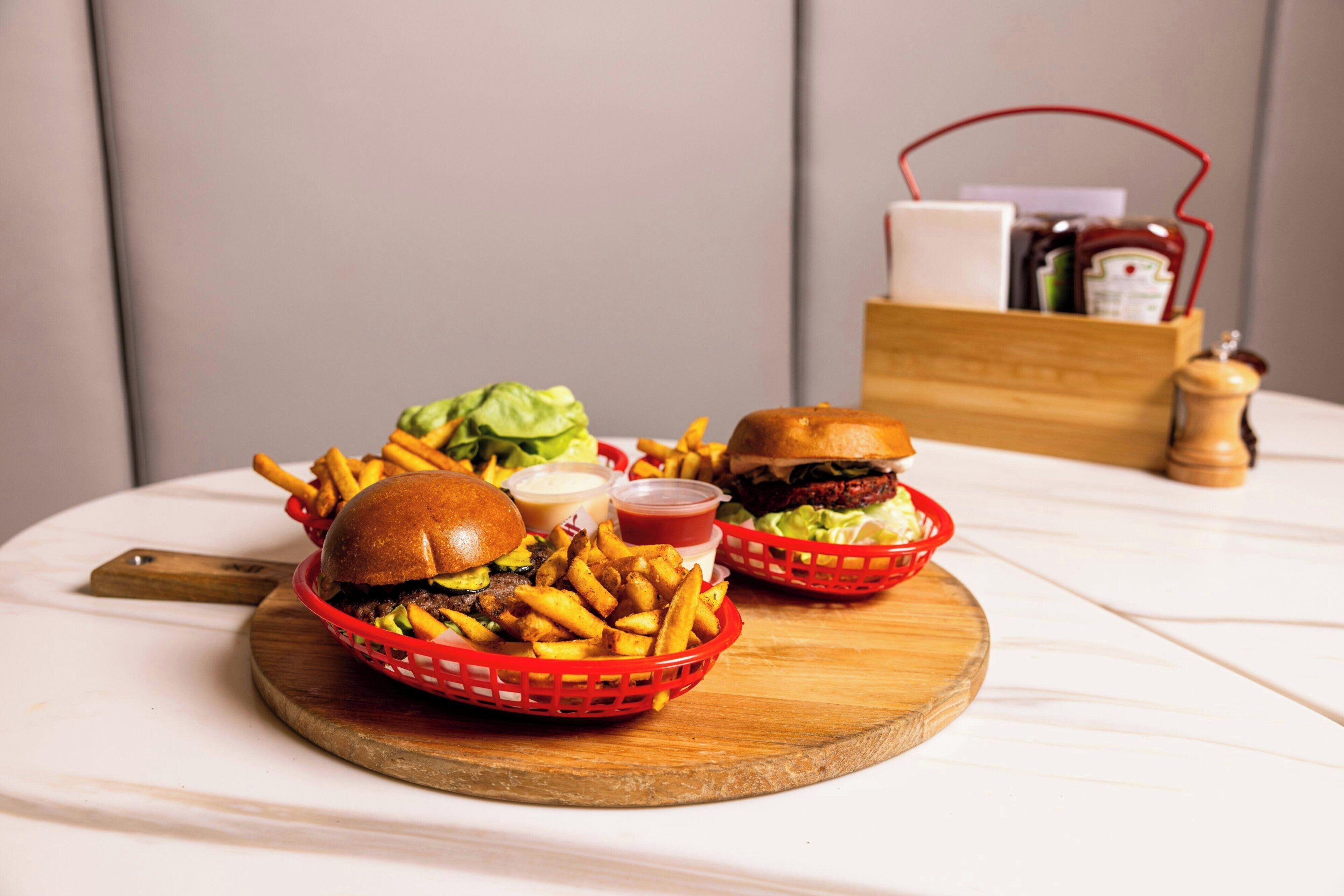 Una mesa de madera con una hamburguesa, papas fritas y un cesto de papas.