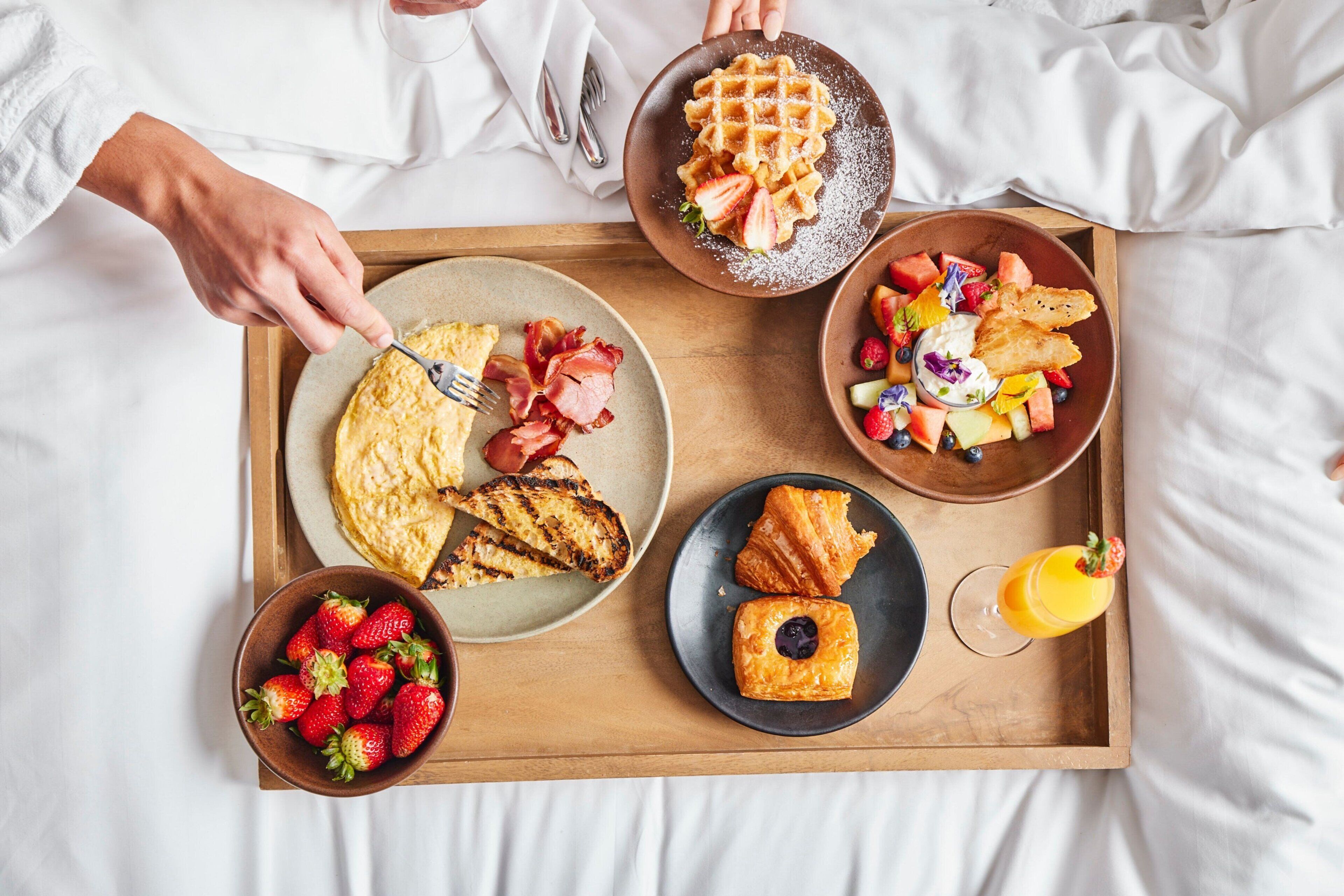 A breakfast tray with waffles, strawberries, a croissant, and a glass of orange juice.