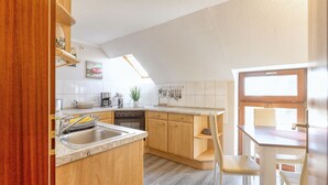 A modern kitchen with wooden cabinets, a built-in oven, and a dining area with a table and chairs. - A beautiful home (Gernrode)