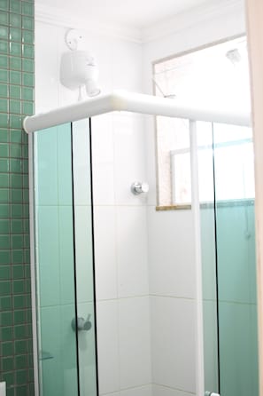Et hjørne af et badeværelse med en glas brusekabine, hvidmalede vægge og et grønt flisepanel.