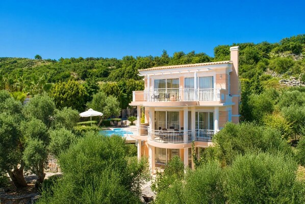 A multi-story building with balconies, a swimming pool, and lush greenery. - Villa Asimenia - Five Bedroom Villa, Sleeps 12 (Agia Triada)