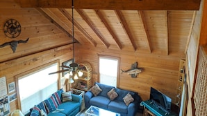 Un interior de cabaña acogedor con techo de madera, un sofá azul, una mesa de centro y un televisor sobre un mueble.