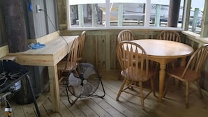 Una cabaña de madera con comedor que incluye una mesa redonda y cuatro sillas, un ventilador y una estufa a gas.
